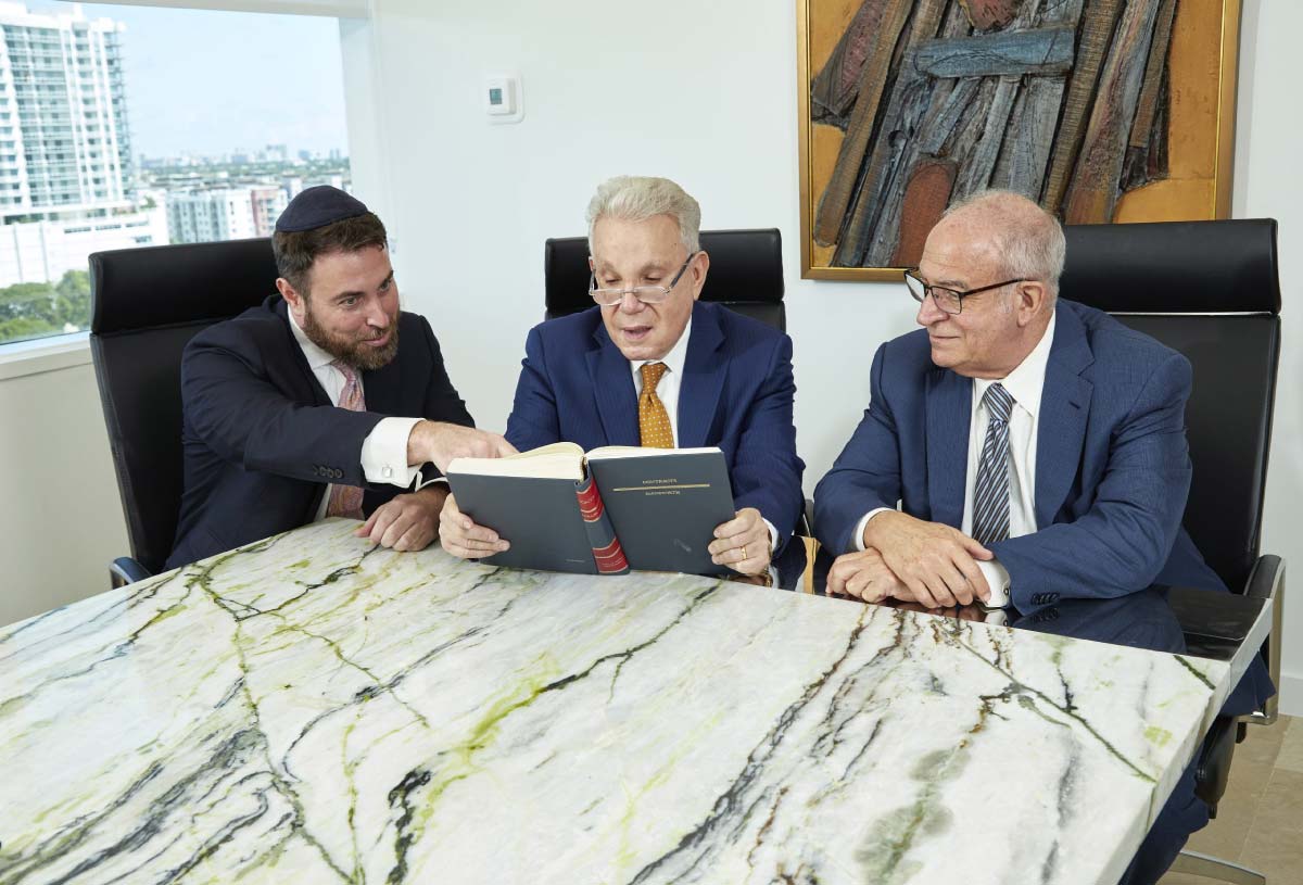 Commercial-Litigation-Law-Firm-Fort-Lauderdale-Partners Three attorneys engaged in discussion over a legal book at a conference table, showcasing collaboration in commercial litigation.
