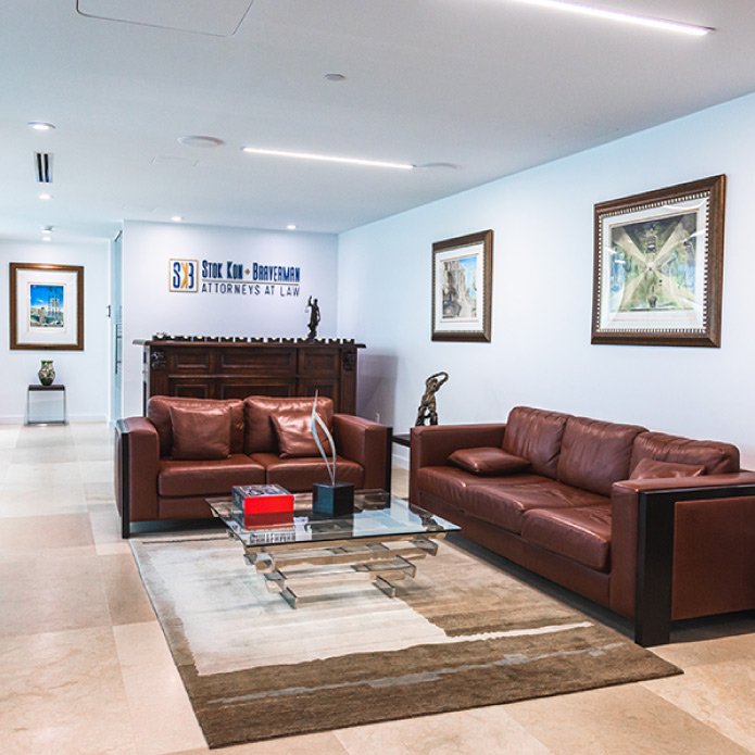 Immigration-Law-Firm-Fort-Lauderdale-Attorney-Office Interior of Stok Kon + Braverman law firm office, featuring leather sofas, glass coffee table, decorative artwork, and firm signage, emphasizing a welcoming atmosphere for family-based immigration consultations.